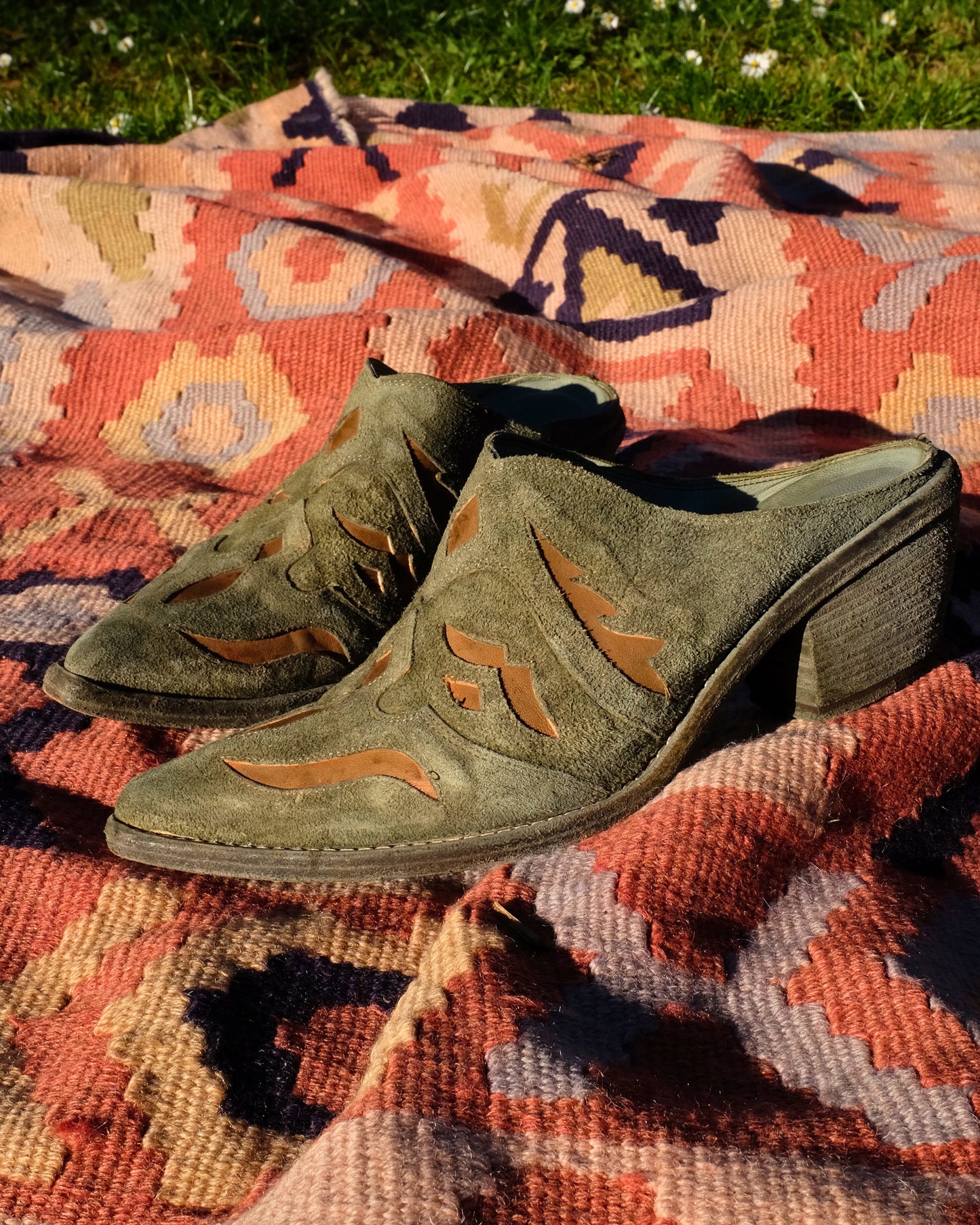Green suede shoes with orange detailing on a patterned rug outdoors.