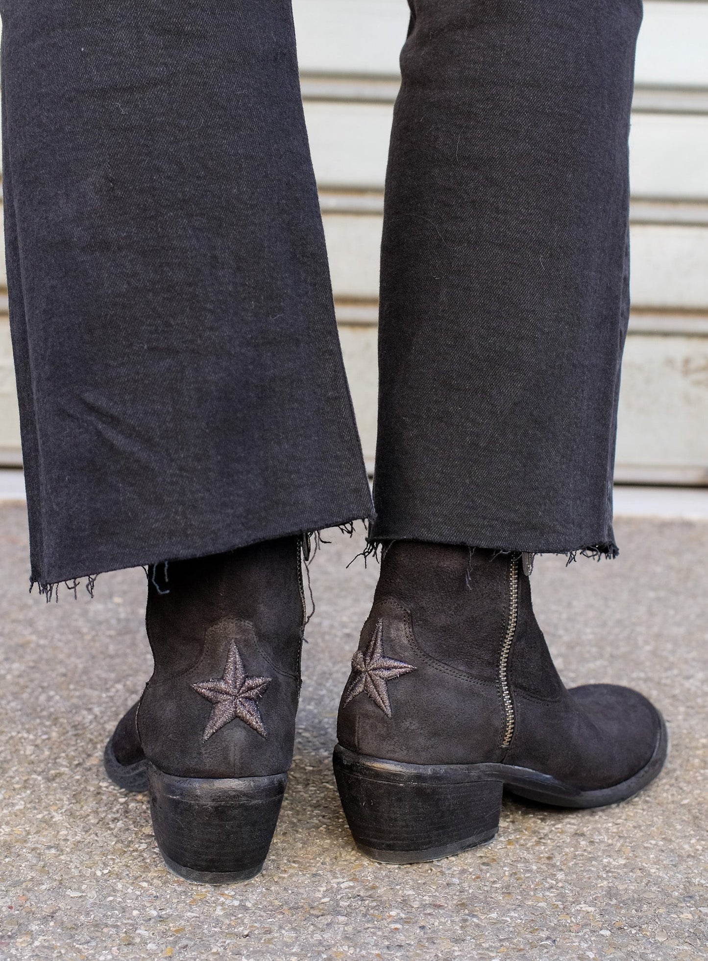Person wearing dark jeans and brown boots with star designs on a concrete floor.