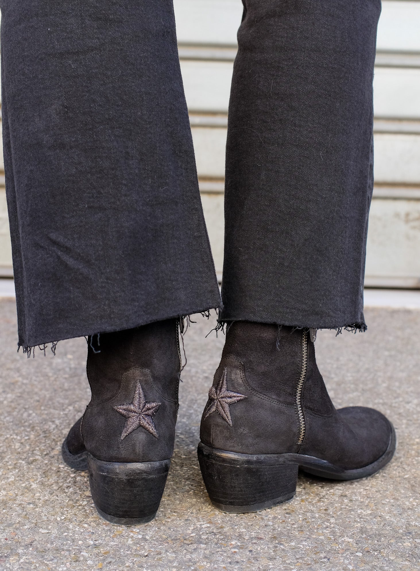 Person wearing dark jeans and brown boots with star designs on a concrete floor.
