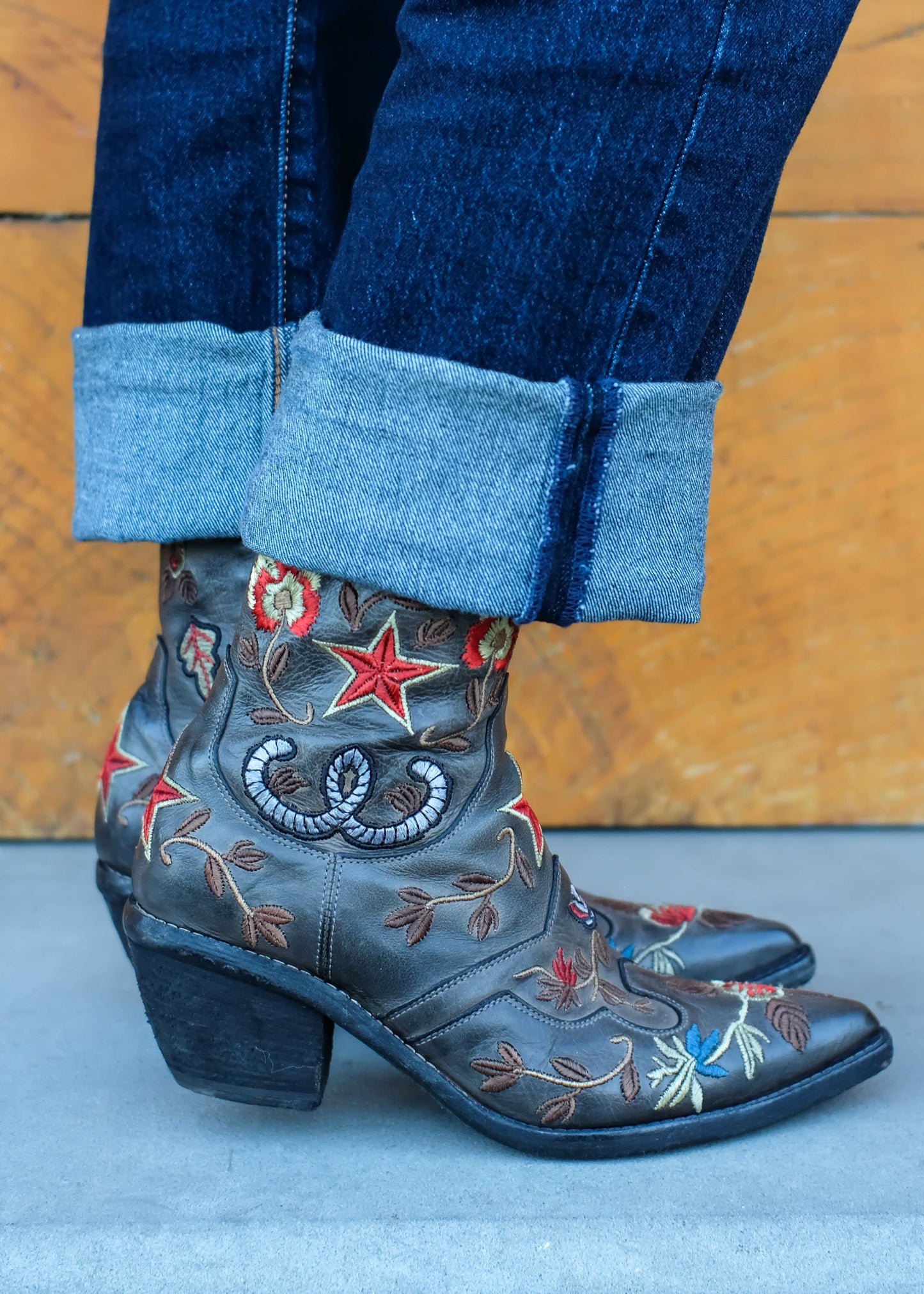 Person wearing blue jeans and embroidered black boots against a wooden background